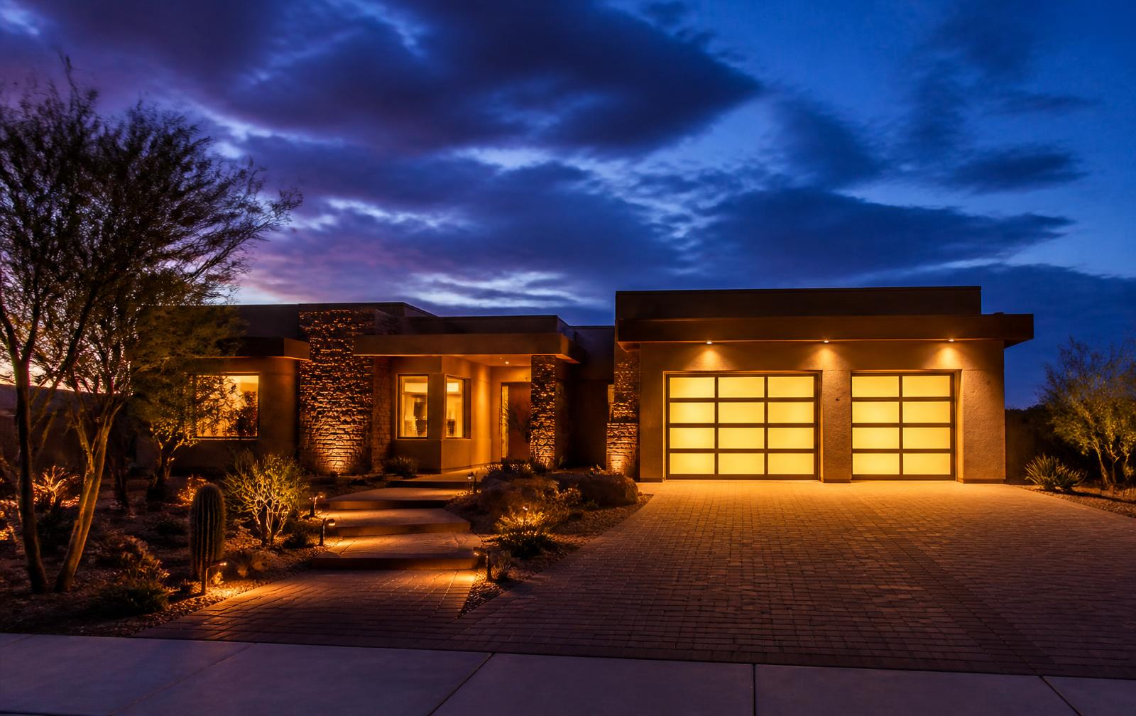 Desert home at dusk with a lit two-car garage